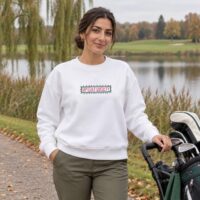 Sweat blanc Octobre Rose Golf Ruban Rose UP Golf Society, porté de face au bord du lac du parcours, chariot de golf à la main